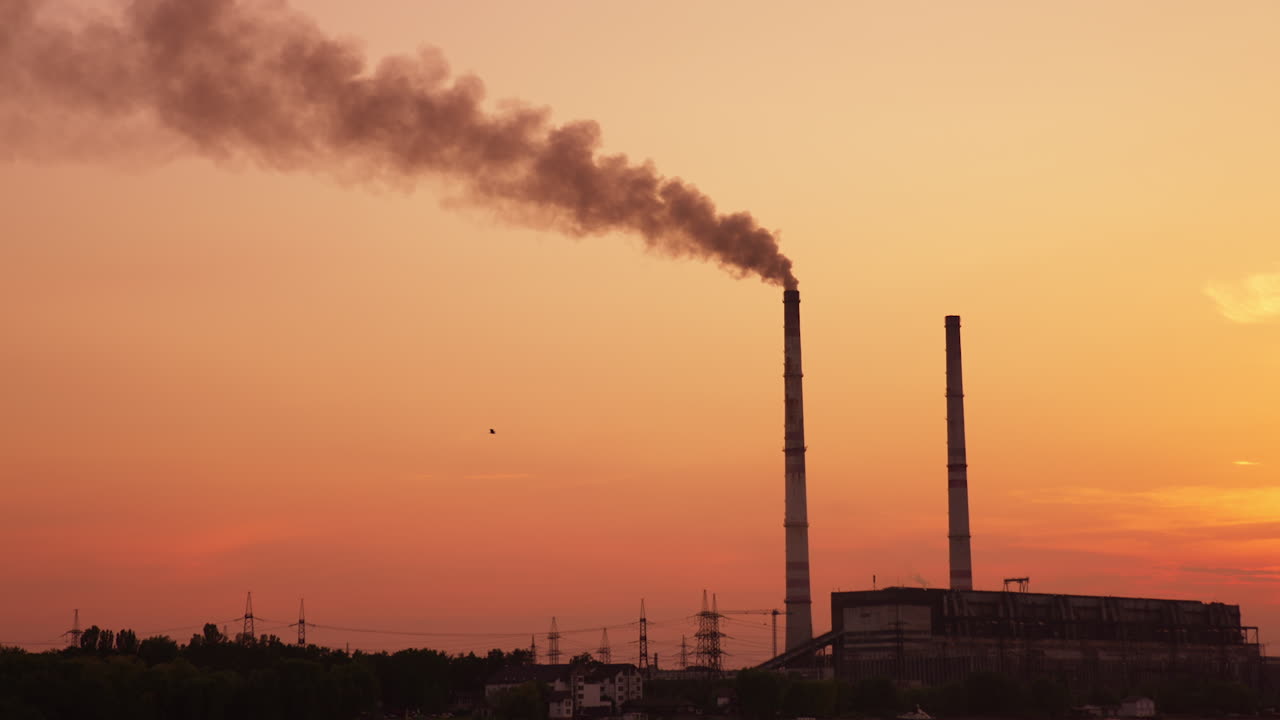 Industrial zone with pipe producing smoke. Plant working at the backdrop of pink sky at sunset. Stork flying in the horizon.