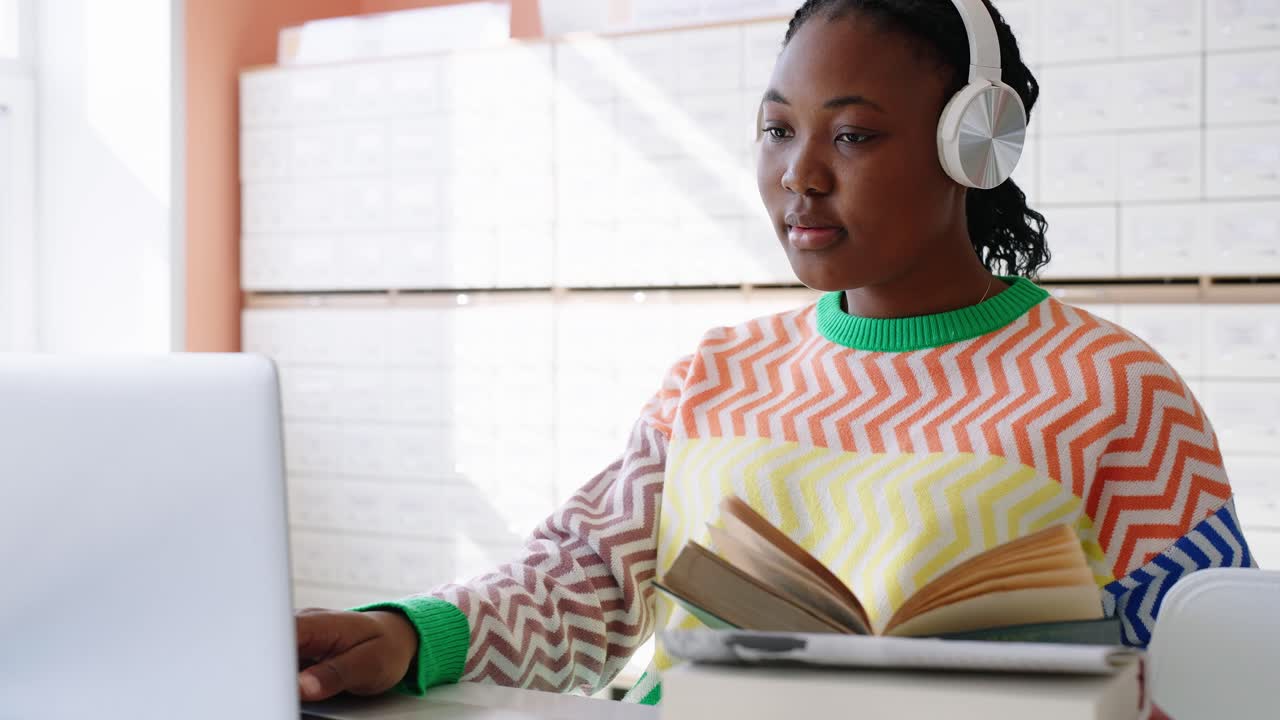 Young Woman Studying with Book and Laptop While Wearing Headphones