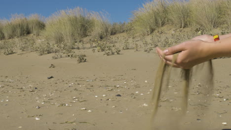 Tiro-Medio-De-Arena-Cae-A-Través-De-Ambas-Manos-De-Una-Mujer-En-La-Playa