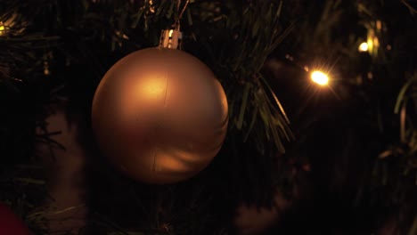 a close-up of a gold bauble ornament hanging on a christmas tree with glowing lights in the background, capturing the festive spirit of the holiday season