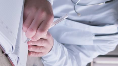concentrated professional young doctor in glasses and uniform is working in his office doing paperwork. writing a diagnosis, treatment plan. a doctor at his workplace. vertical video