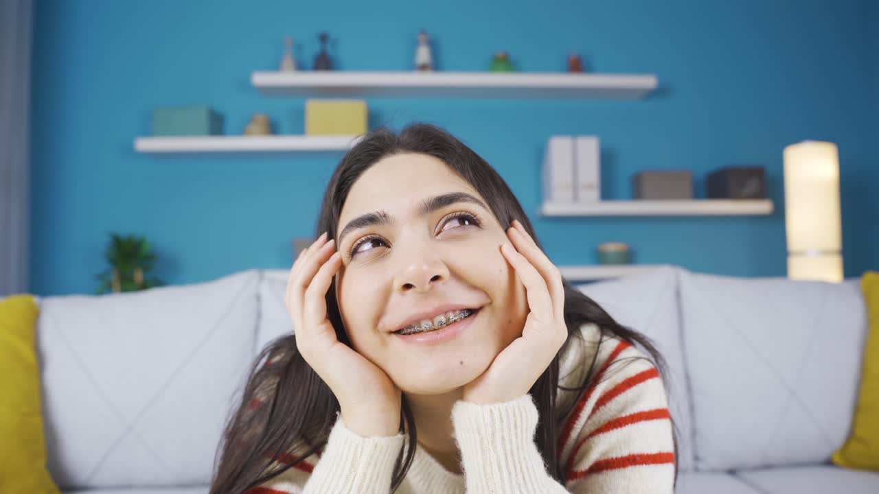 집에서 혼자 앉아서 행복한 순간들을 생각하고 미소 짓는 젊은 여성.