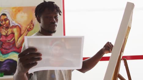 african american male painter painting from photograph on canvas in artist studio