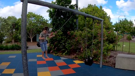 a happy young child smiling and waving while swinging in a park