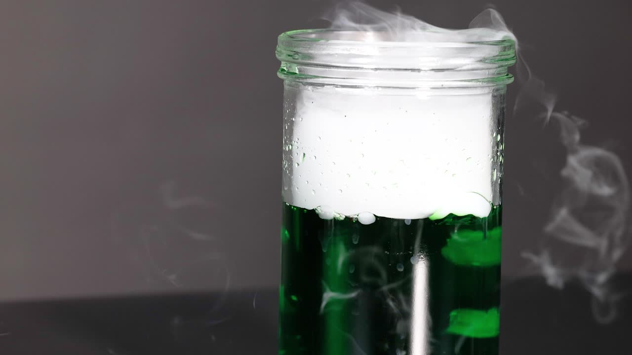 녹색 액체가 반응하여 연기와 거품을 생성합니다.