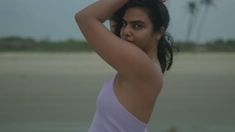 a confident woman in a lavender dress poses on the beach at dusk, her eyes fixed on the camera. the soft light and tranquil setting enhance her striking presence. india