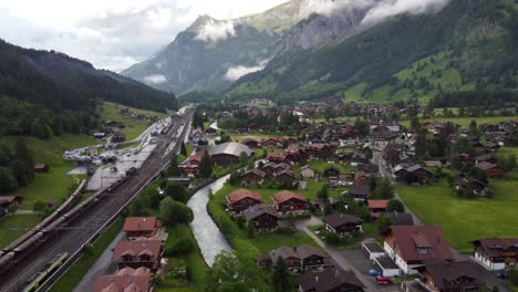 descendiendo hacia atrás paisaje urbano aéreo: el tren pasa por la estación junto al glaciar alpino que fluye desde los alpes suizos a través de la aldea suiza de kandersteg en bluemlisalp famosa por el lago oeschienensee