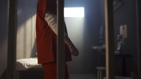 arrested woman in handcuffs walking behind bars in prison cell