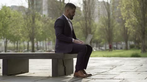 Handsome-businessman-using-laptop-on-street