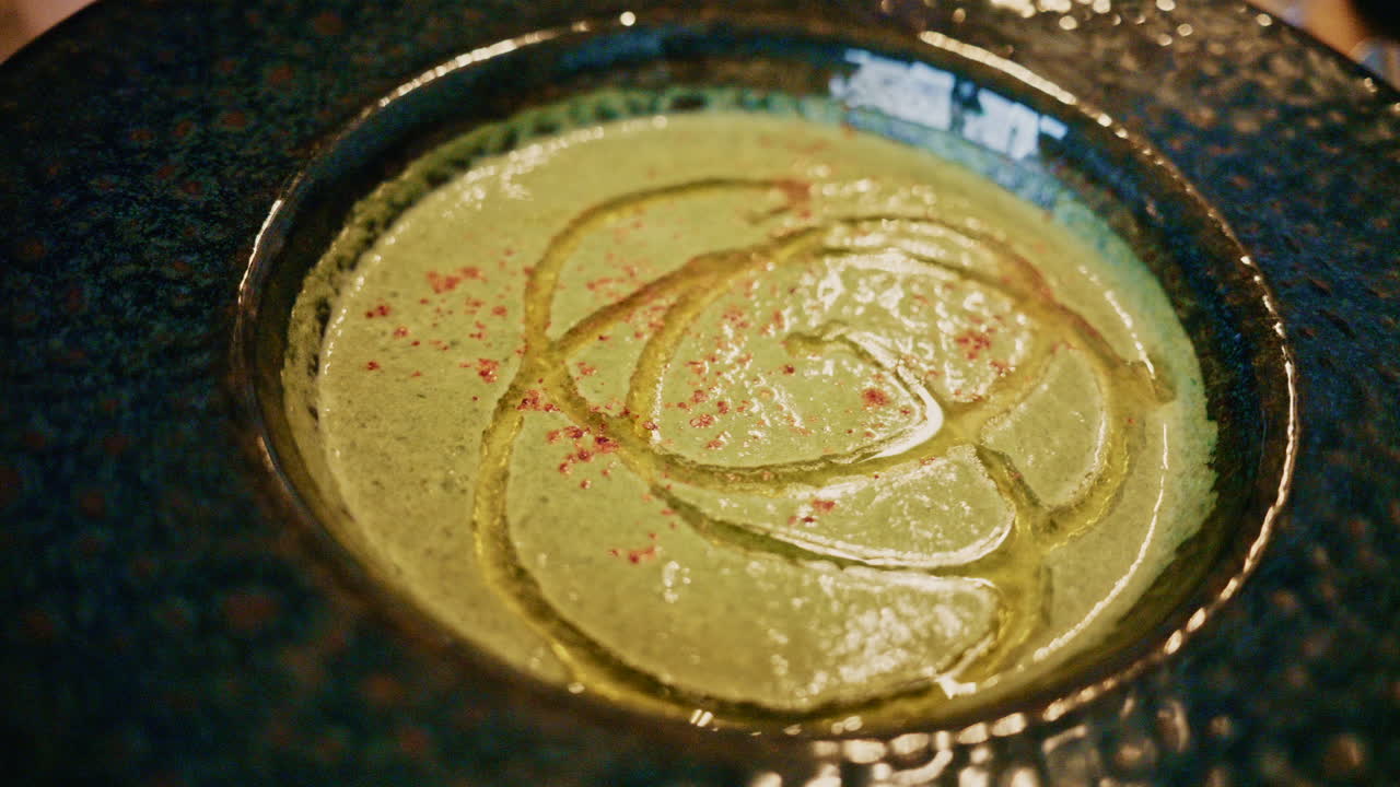 Top view of a creamy green soup garnished with oil and spices, served in a ceramic bowl on a wooden table