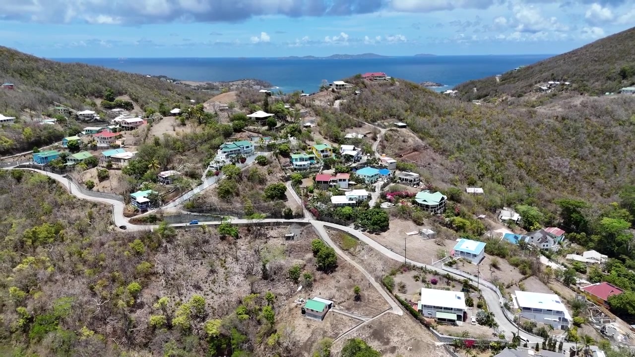 Vuelo de dron sobre pueblos costeros en ladera, carreteras locales y exuberante terreno tropical en la isla de Bequia, San Vicente y las Granadinas