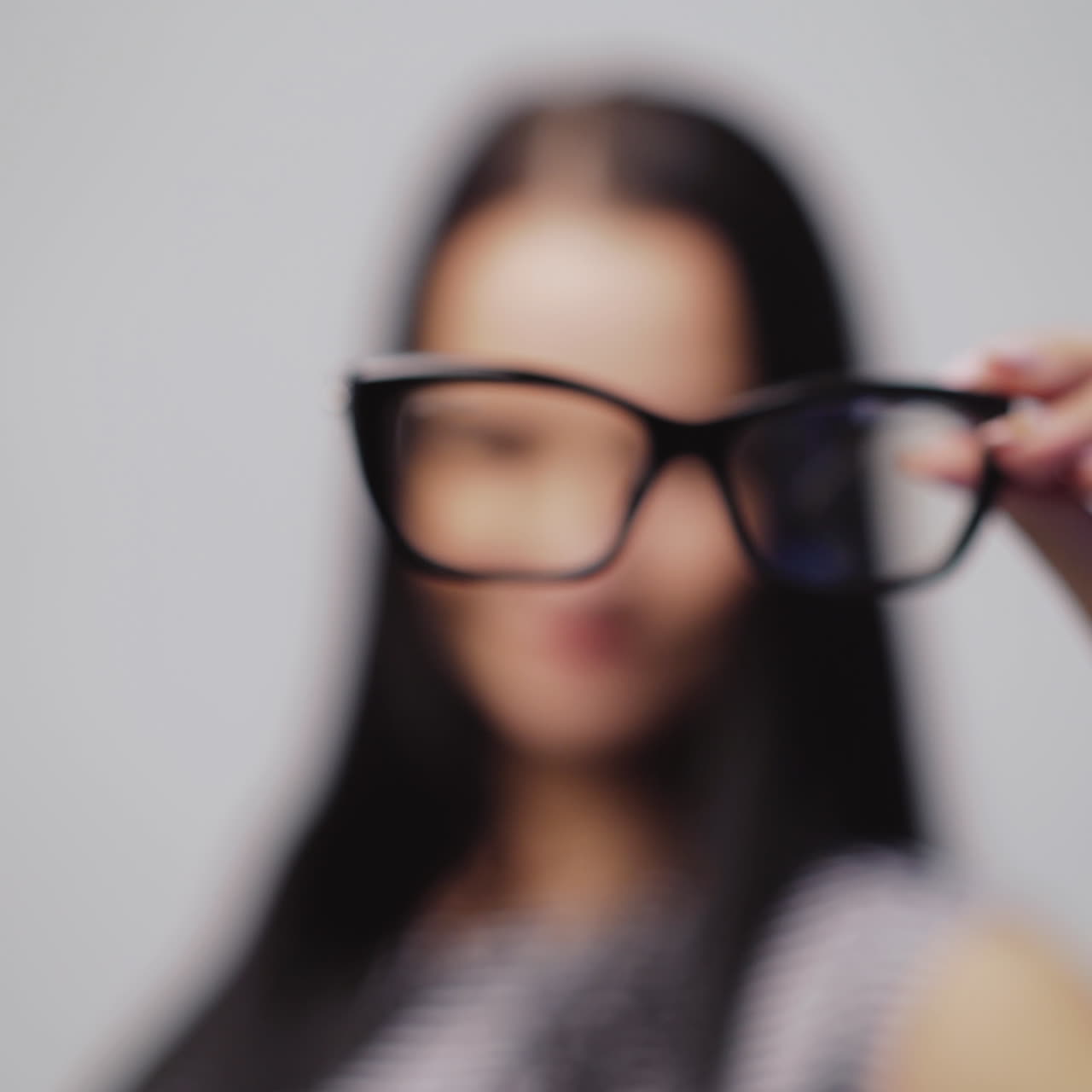 Attractive young woman in stylish eyeglasses removes them to the camera close-up. Pretty female with glasses for vision on the grey background.