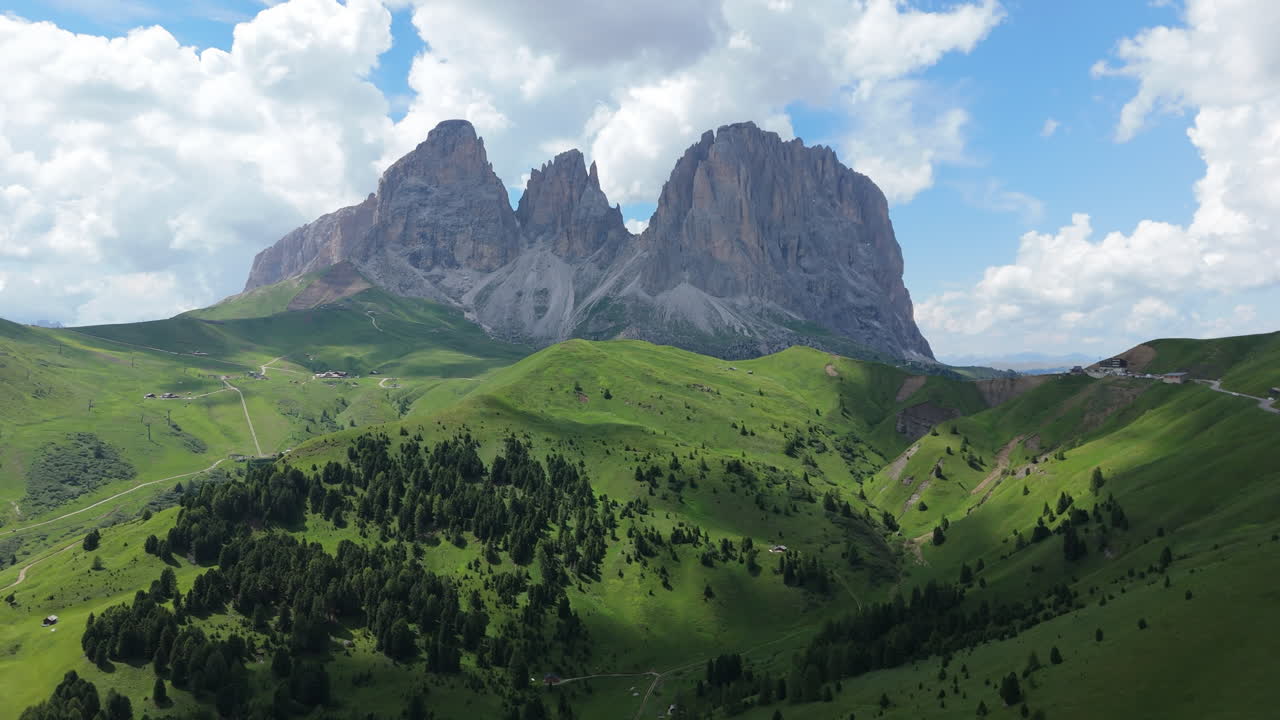 Majestic Dolomites mountains under drifting summer clouds, captured by drone in clear alpine air with vibrant green slopes