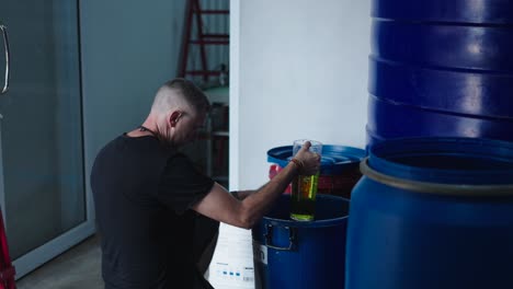 worker pouring liquid into large blue barrel