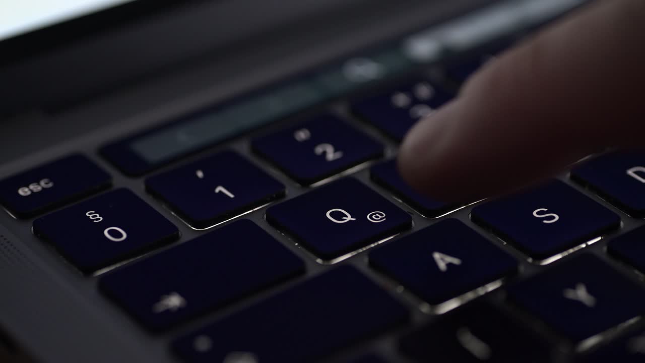 A close-up video of a finger pressing the Q key on a laptop keyboard. The dark keys and shallow depth of field create a focused and professional atmosphere