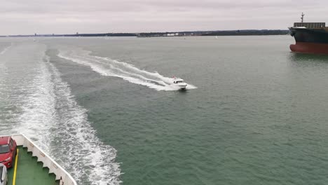 un barco rápido y caro que intenta pasar un gran ferry que va de southampton a east cowes, en un día gris y nublado en medio de la nada
