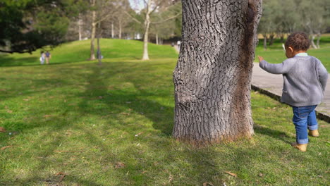 niño corriendo alrededor del árbol, jugando al escondite, sonriendo