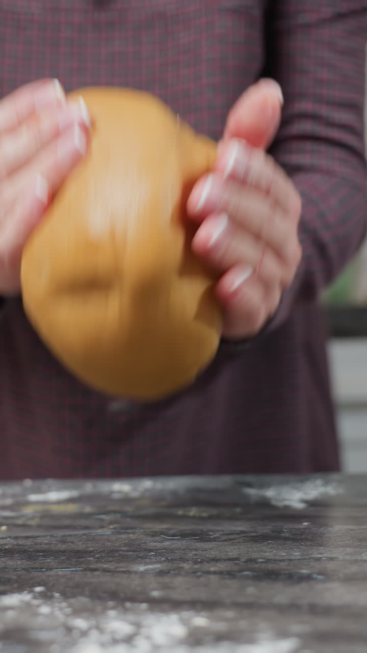 Close up of woman kneading dough, lifting it, and dropping it on kitchen table, hands in motion, flour dust on surface, soft dough bouncing, warm kitchen setting with modern cabinets in background