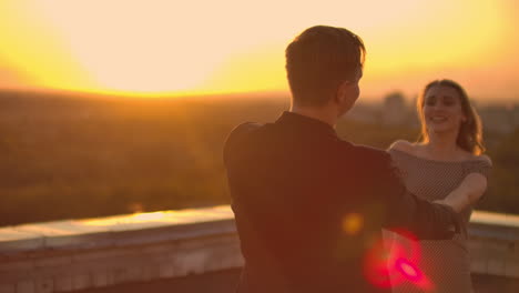 dos amantes, un hombre y una mujer, se ríen y bailan en el techo al atardecer.