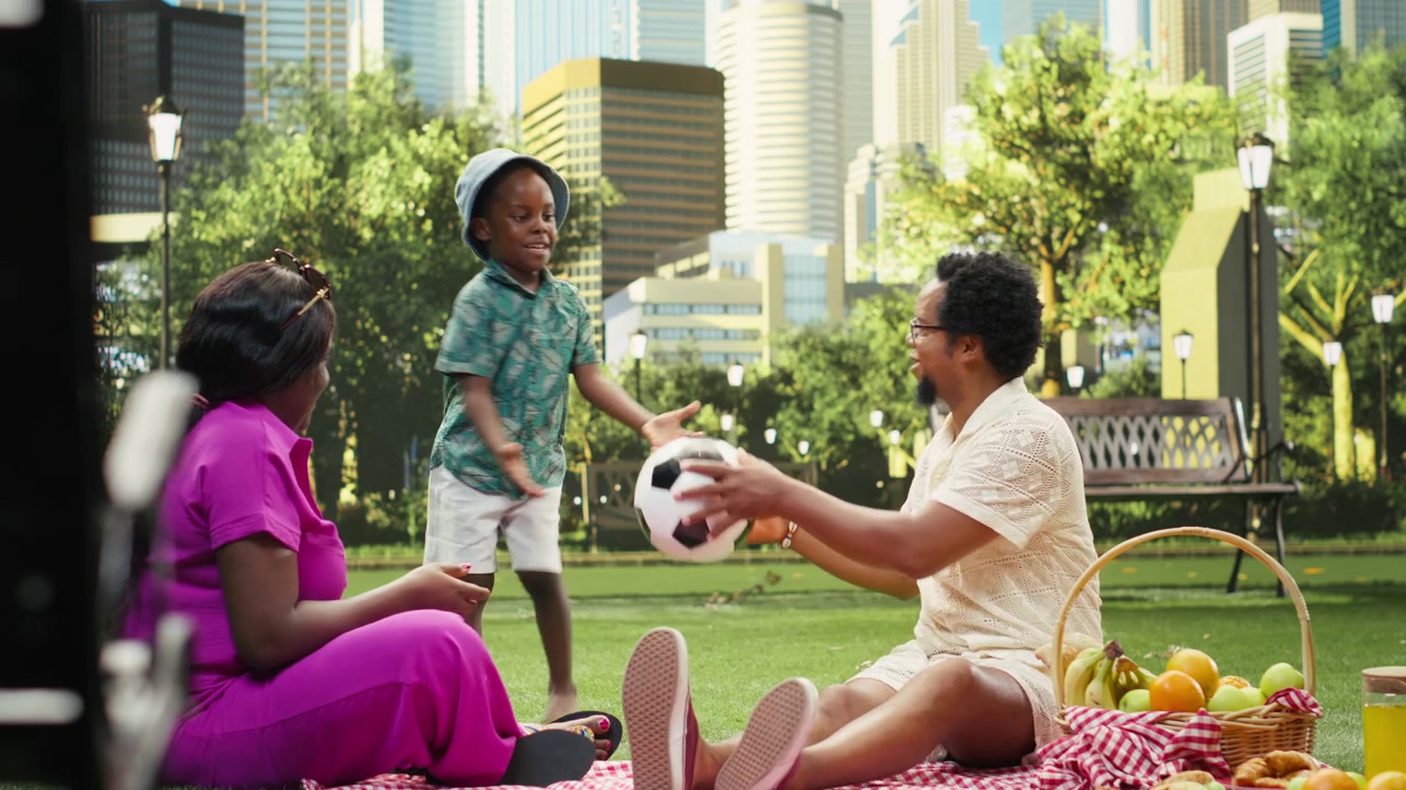 Parents and boy playing catch with soccer ball beside picnic basket