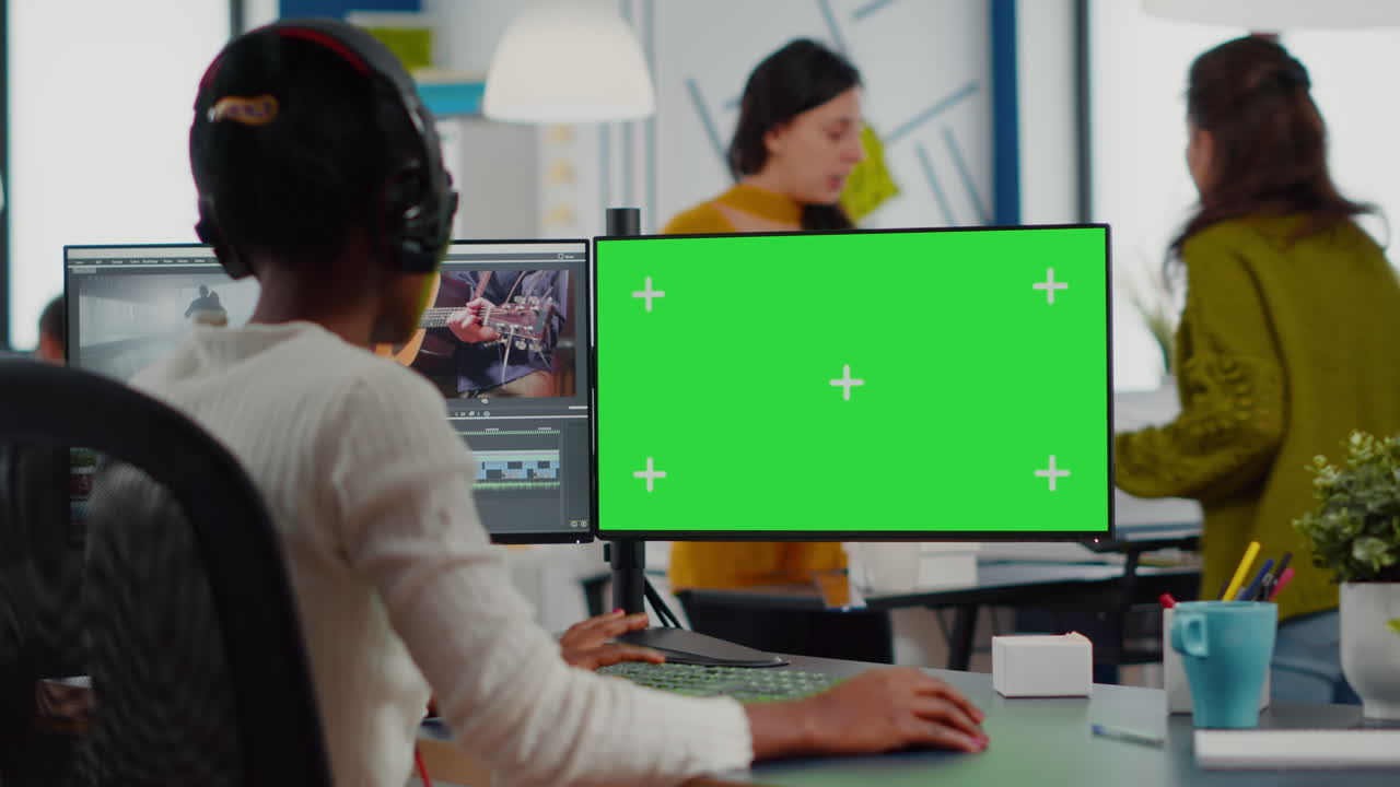 videografo nero con cuffie che usa un computer con schermo verde