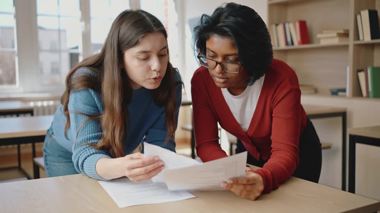 Vertical video: Getting papers, two peers scanning sheets for class at study desk, one with glasses