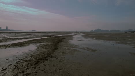 Low-drone-shot-flying-over-muddy,-wet-terrain-during-beautiful-blue-hour-dusk-sunset