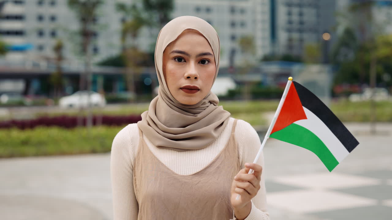 Woman in hijab holding Palestinian flag in city