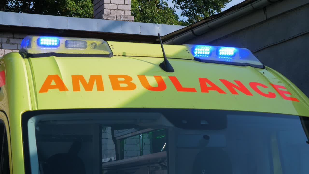 Taget af en gul paramedicinerambulance parkeret udenfor, blå blinkende advarselslys, solrig dag, mellembillede