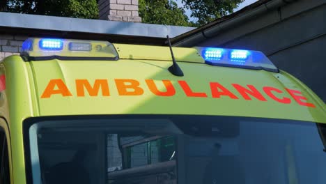 the roof of yellow paramedic ambulance vehicle parked outside, blue flashing warning lights, sunny day, medium shot