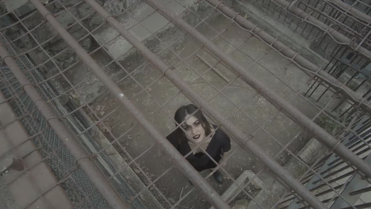 Young adult woman goth dressed all black waiting in a cage overhead angle