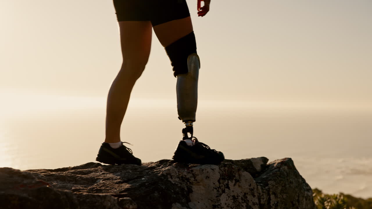 Woman with prosthetic leg hiking on a cliff overlooking the ocean at sunrise/sunset.