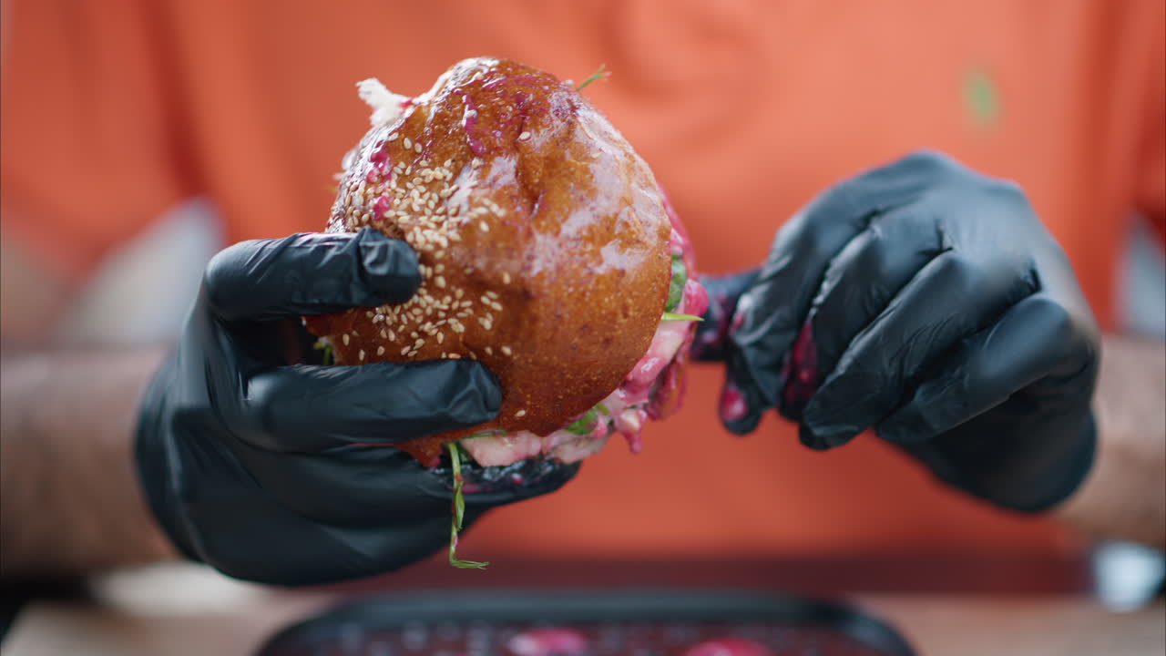 Man eating a burger with red sauce, black gum gloves, close up