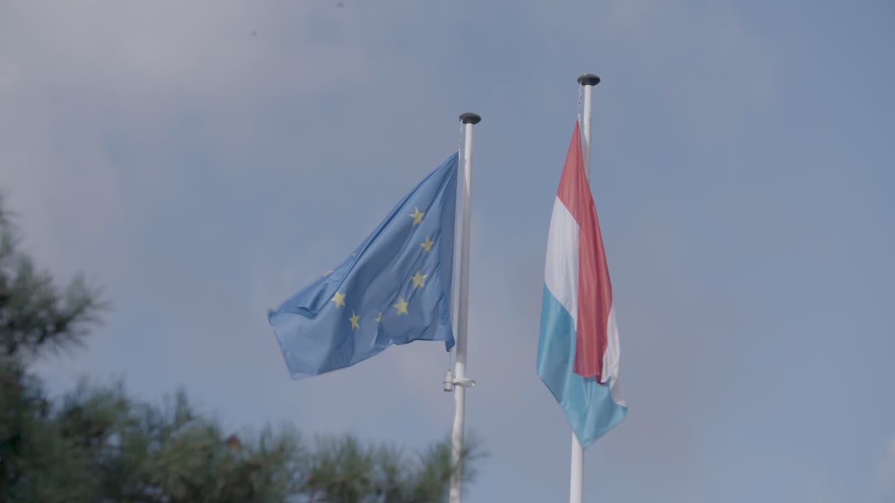 Bandiere dell'Unione Europea e del Lussemburgo che sventolano contro un cielo blu con nuvole