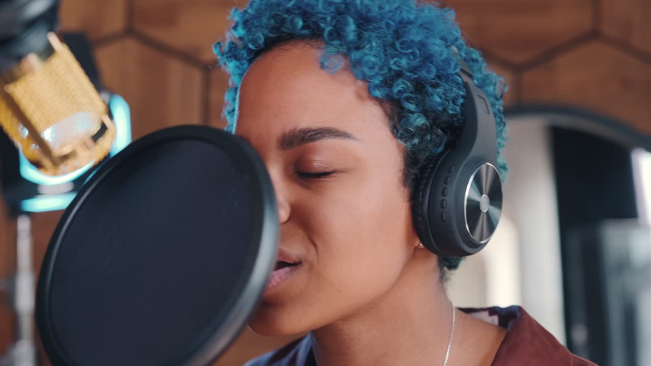 젊은 아프리카계 미국인 여성 가수가 마이크를 사용하여 팝 노래를 녹음합니다.