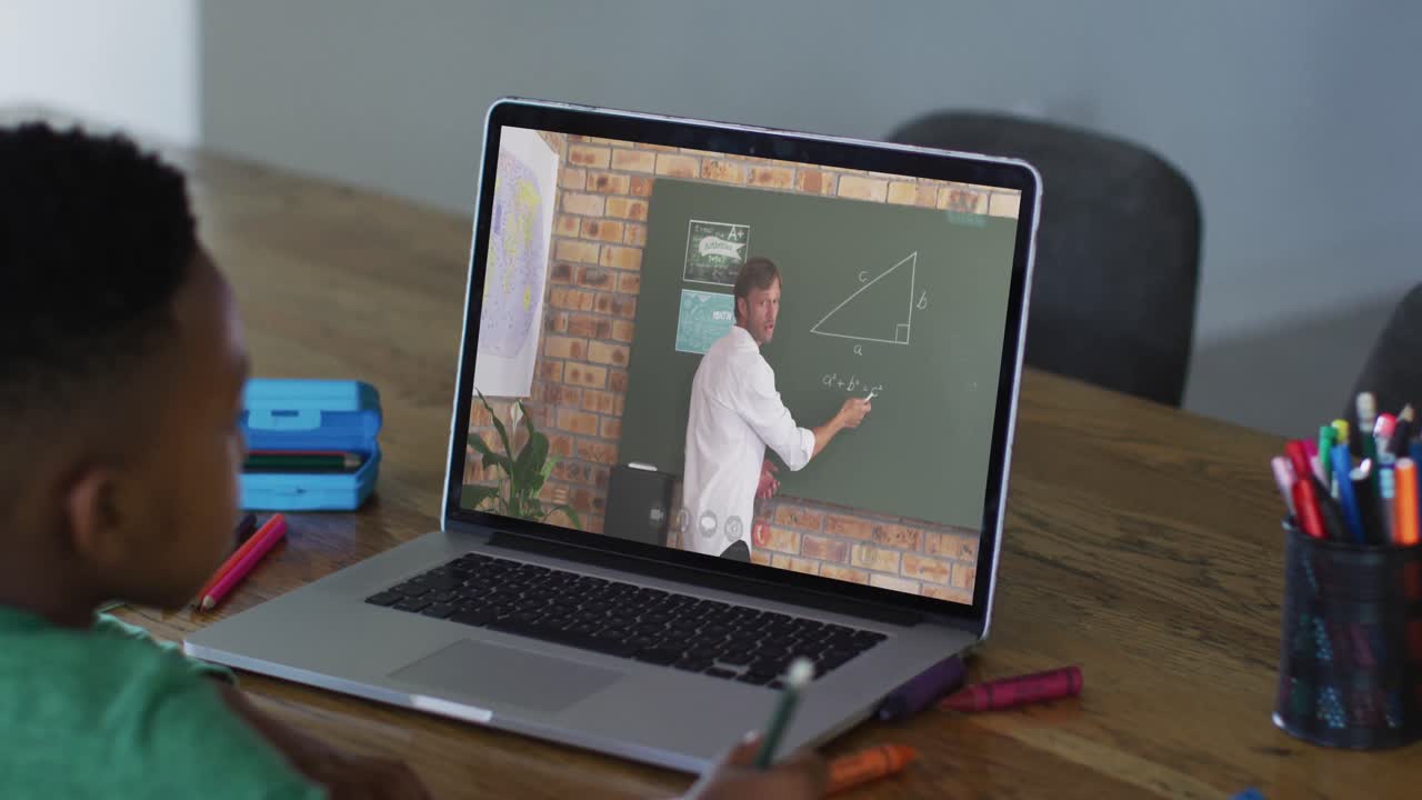 niño afroamericano haciendo la tarea mientras tiene una videollamada con un profesor masculino en una computadora portátil en casa
