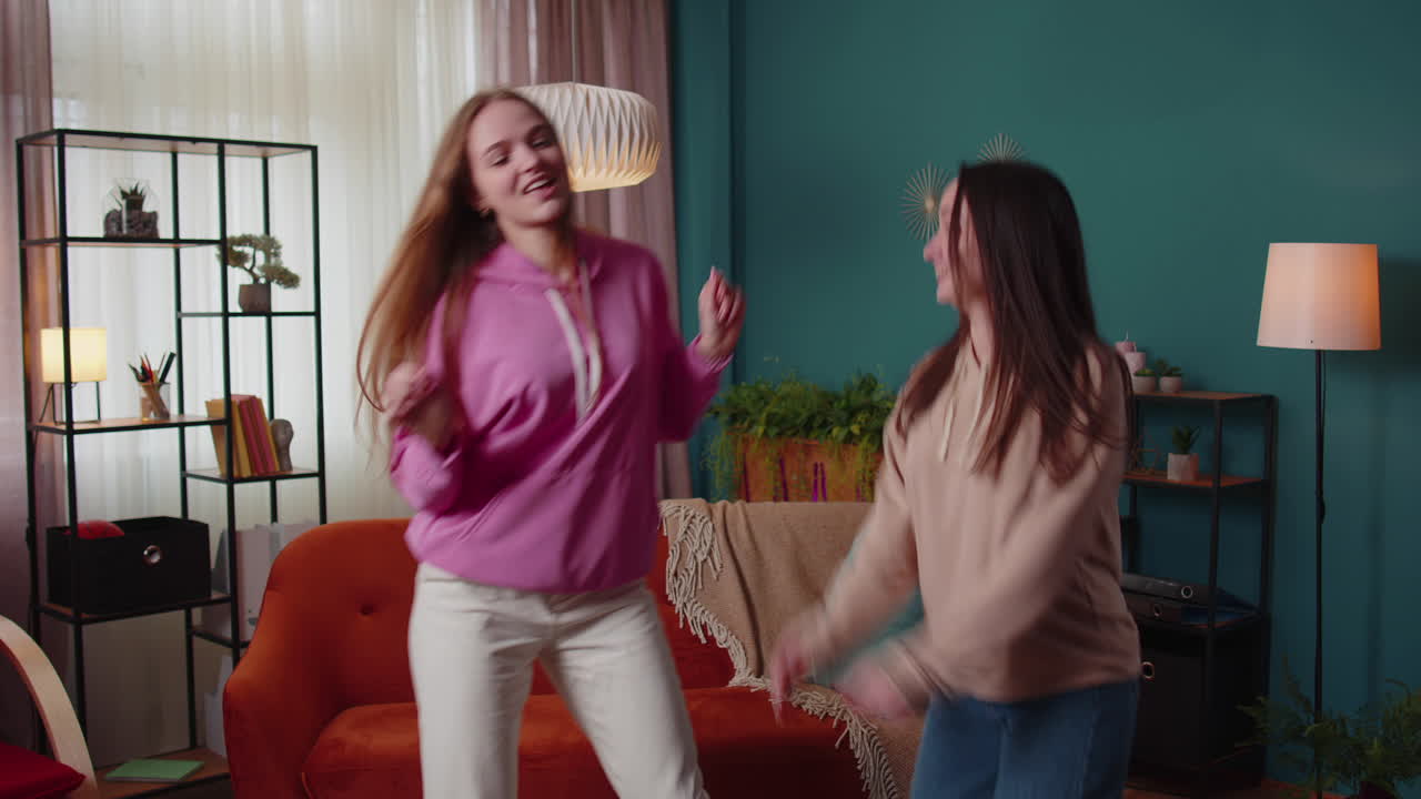 Happy two teenage girls siblings or bloggers couple dancing at home having fun enjoying trendy dance