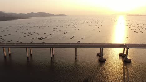 Traffic-on-Hong-Kong-Shenzhen-Bay-Bridge-at-Sunset,-with-Fish-and-Oyster-cultivation-pools,-Aerial-view