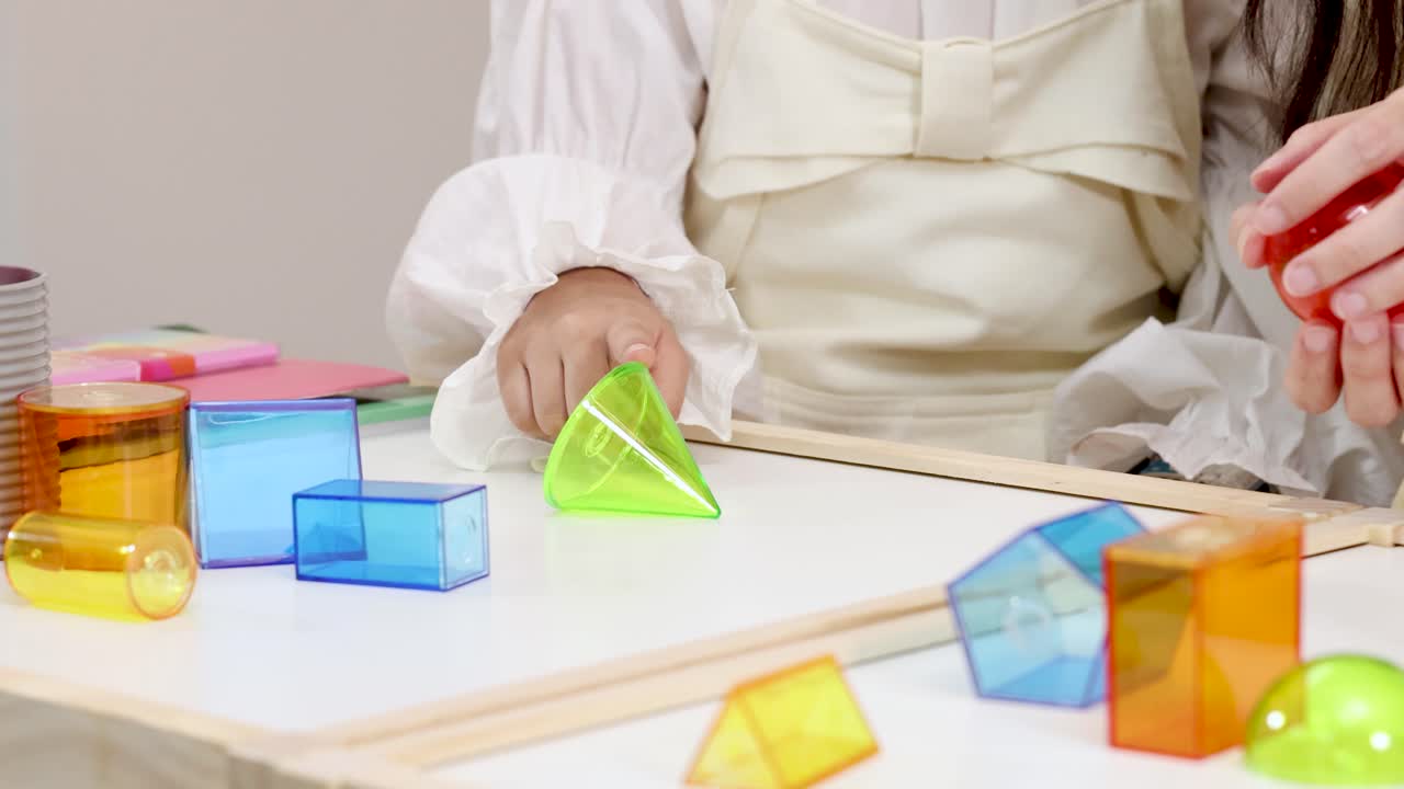 Two people manipulate translucent geometric solids under soft lighting, emphasizing math education and interaction