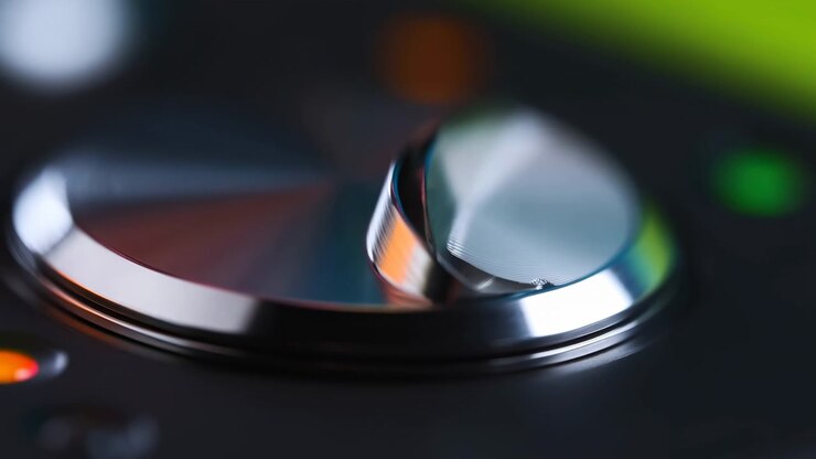 Raised metallic curve gradually settles closer to round base as bright reflections slide across smooth silver surfaces, surrounded by dark housing and blurred green and orange lights.
