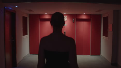 woman walking through a dark hallway with red elevator doors