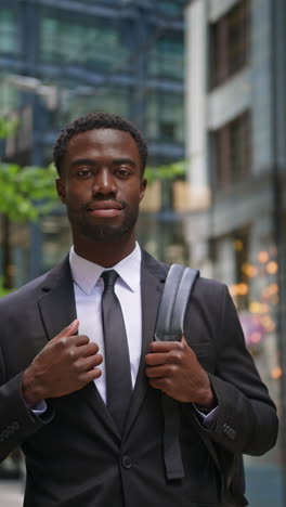 vertical video portrait of confident young businessman wearing suit standing outside offices in the financial district of the city of london uk shot in real time