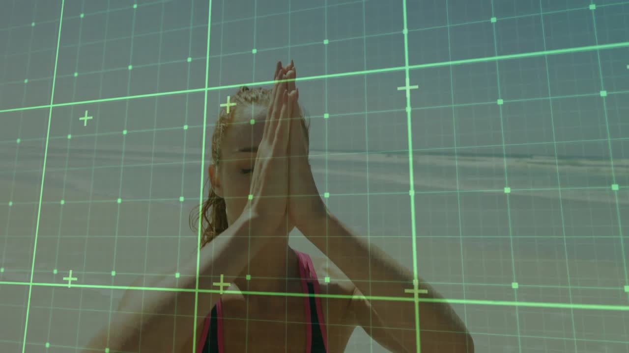Woman seated on beach, drawing breath, lifting arms into prayer under green grid for fitness