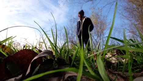 un hombre solo borroso que usa gorro y abrigo en el soleado día de invierno caminando hacia la cámara en un campo de hierba verde con cielo azul en un paseo al aire libre en el campo rural