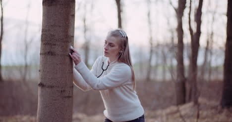 woman uses a stethoscope and examines a tree in the forest 2