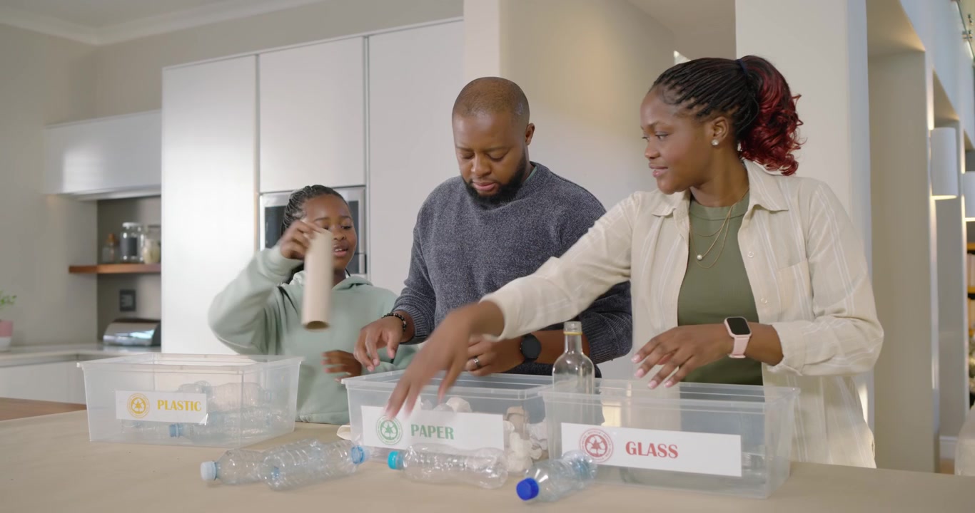 African American family sorting recyclables at kitchen island, daughter bringing bins to recycle