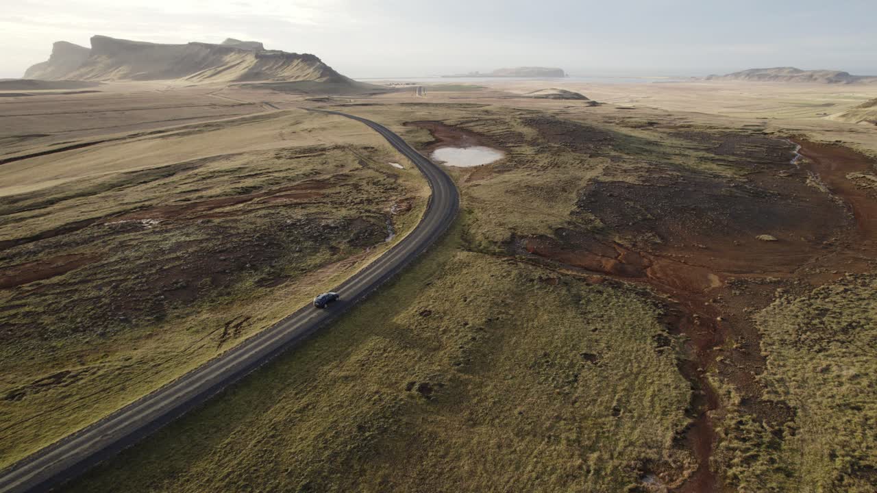 aerial siguiendo el coche negro conduce a través de la vasta panorámica de las montañas volcánicas de islandia