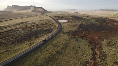 aerial following black car drive through vast iceland volcanic mountain panorama