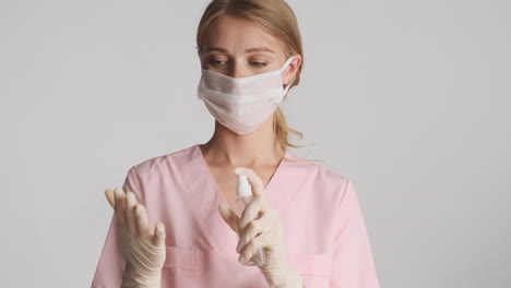 Caucasian female doctor in medical gloves and mask using hand sanitizer.