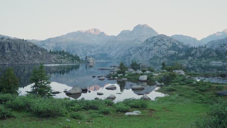 serene mountain lake at dawn with still waters reflecting rocky peaks and green landscape